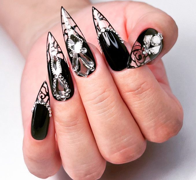 Ilgi juodi stiletto nagai su ryškiu kristalų dekoru – efektingas, bet ne elegantiškas pasirinkimas.